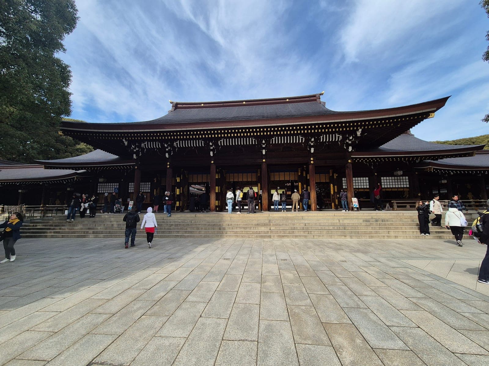 La fachada del salón principal del santuario Meiji Jingū, con su gran techo curvo de tejas oscuras y visitantes subiendo las escaleras hacia la entrada