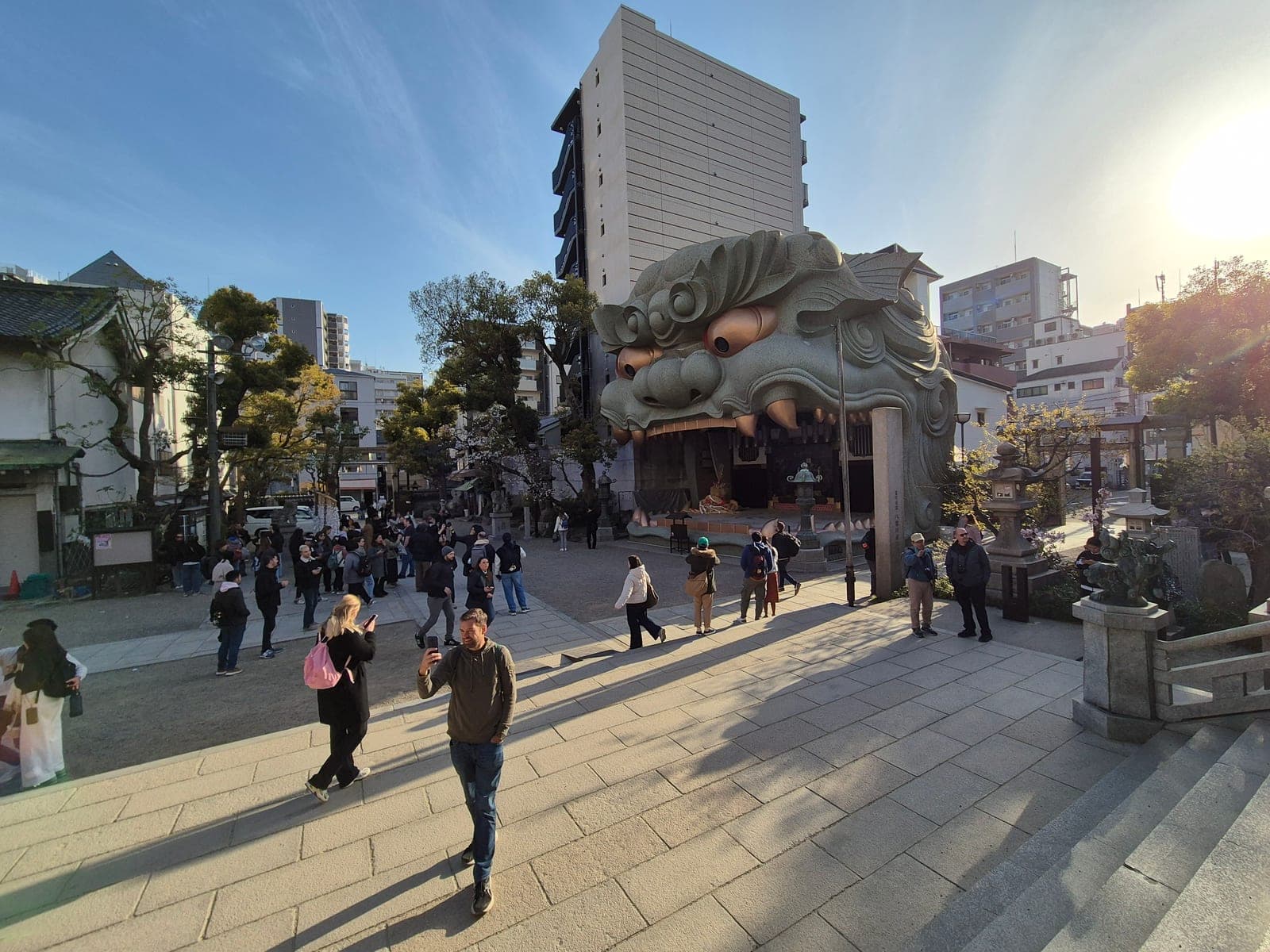 La fachada del santuario Namba Yasaka en Osaka, dominada por una escultura gris verdosa de una cabeza de león gigante que funciona como escenario, con turistas tomando fotos