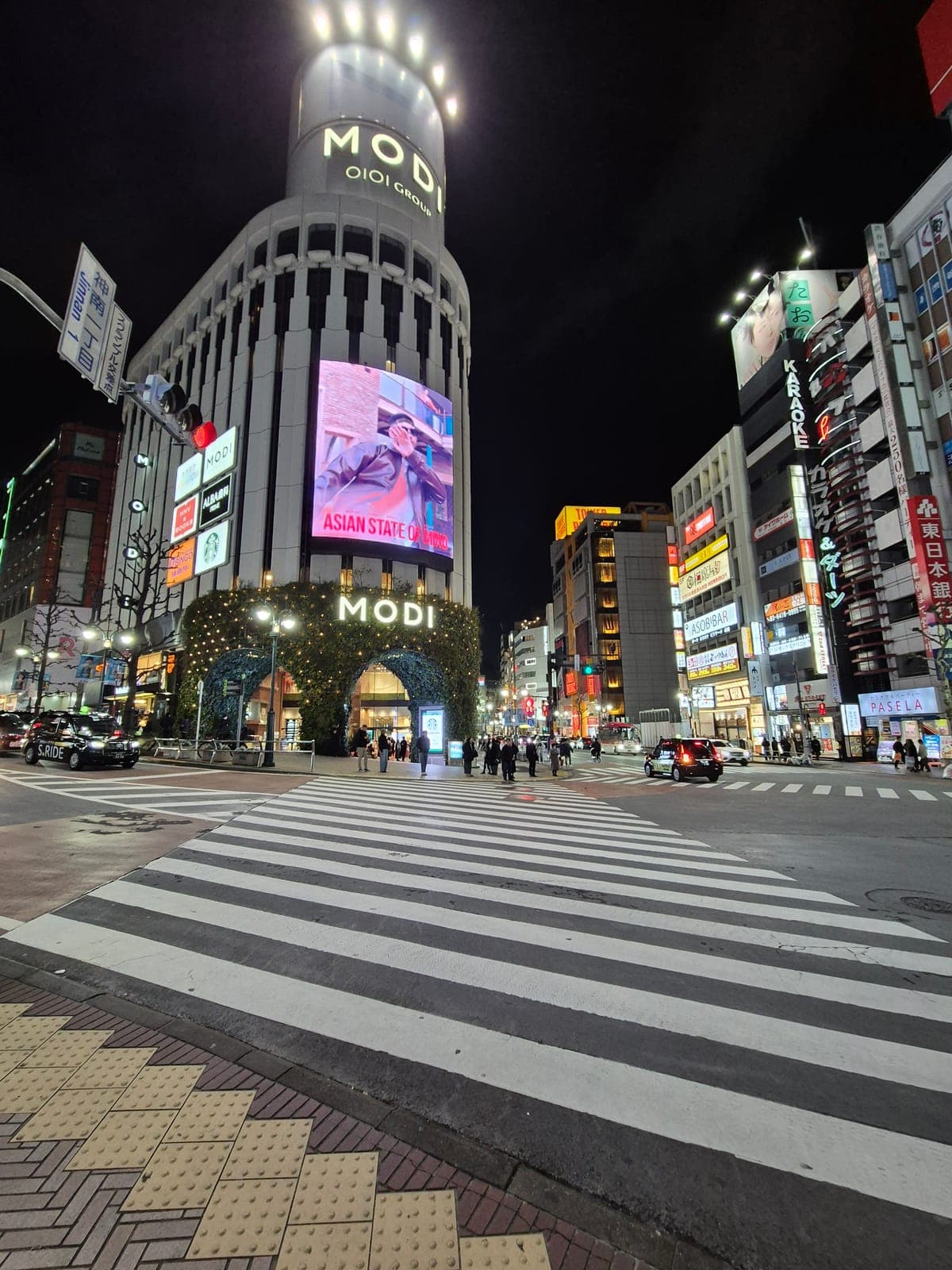 El edificio MODI en Shibuya iluminado de noche, con anuncios luminosos y la calle Jinnan al frente