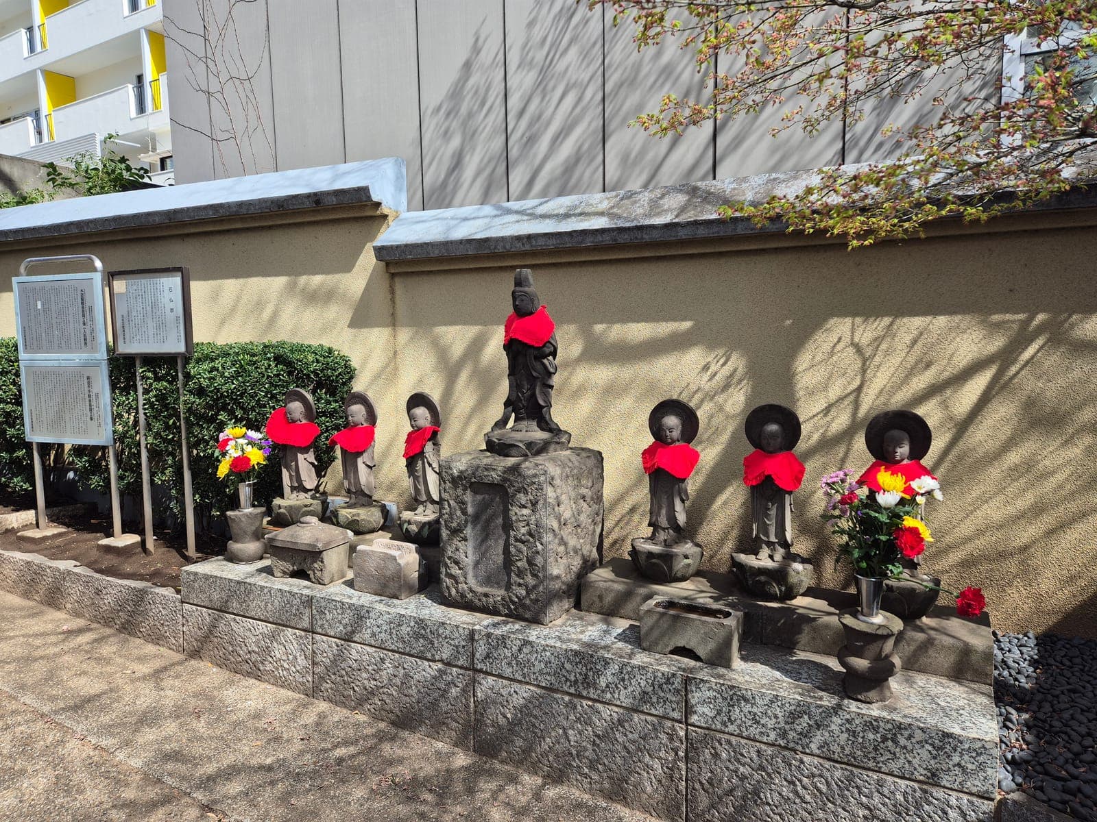Fila de estatuas jizō con baberos rojos en el pequeño templo Chōsen-ji de Shibuya, rodeadas de flores