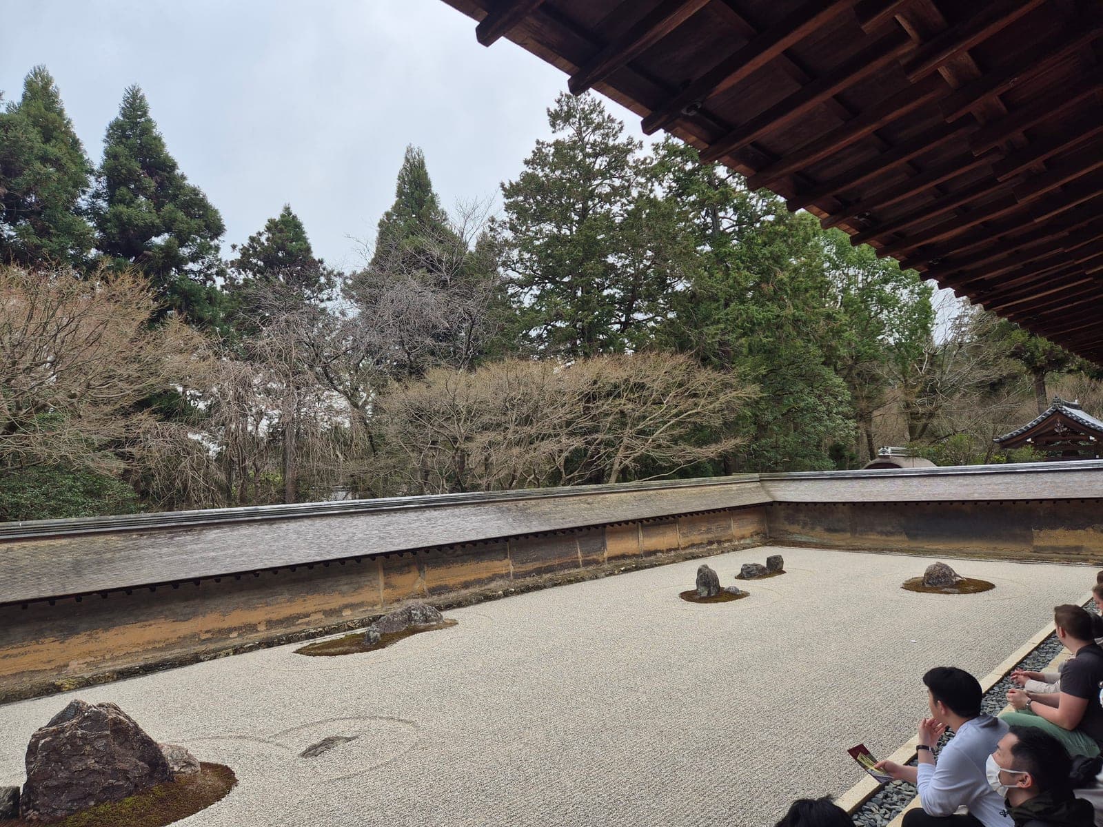 Visitantes sentados en la galería de madera del Ryōan-ji contemplando el jardín seco de piedras y grava rastrillada