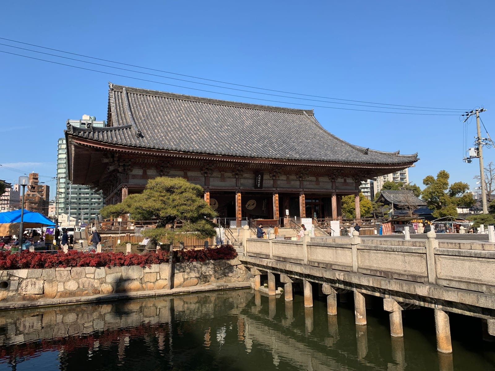 El estanque del Shitennōji con su puente de piedra sobre pilares, frente a uno de los grandes salones de madera del templo, en un día despejado