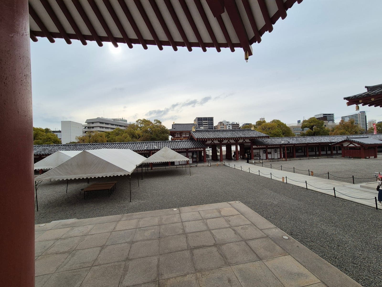 El patio central de grava del templo Shitennōji, visto desde el corredor techado, con carpas blancas instaladas y el salón principal al fondo bajo un cielo nublado