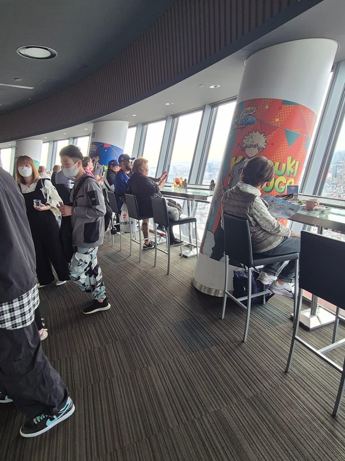 Zona de descanso con publicidad de un anime dentro de una de las tiendas de Tokyo Skytree, con visitantes sentados junto a los ventanales