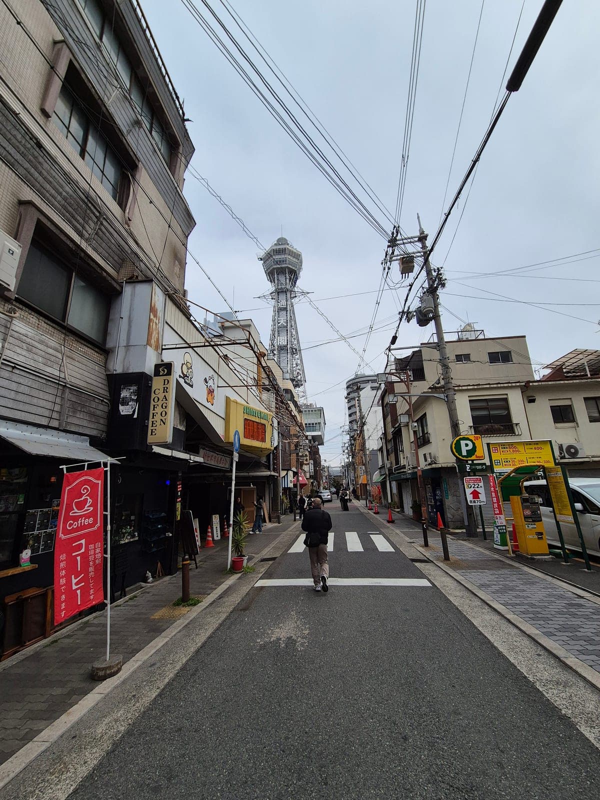 La torre Tsutenkaku vista de frente al final de una calle de Shinsekai en Osaka, con negocios y cableado eléctrico a los lados